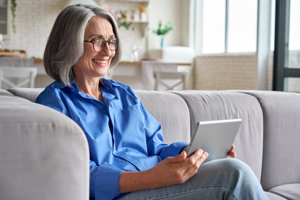 Senior woman sitting on couch smiling while using a tablet
